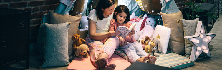 Mother and daughter having a pajama party reading a book in a diy tent © David Pereiras