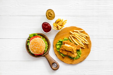 Burger served with french fries and fried chicken on wooden board. Top view