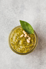 Pesto sauce in a jar with pine nuts and green basil leaves. Top view. Copy space.