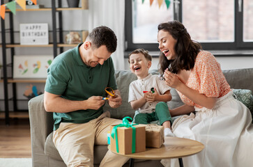 family, holidays and people concept - happy mother, father and little son with gifts and party blowers having fun and celebrating birthday at home