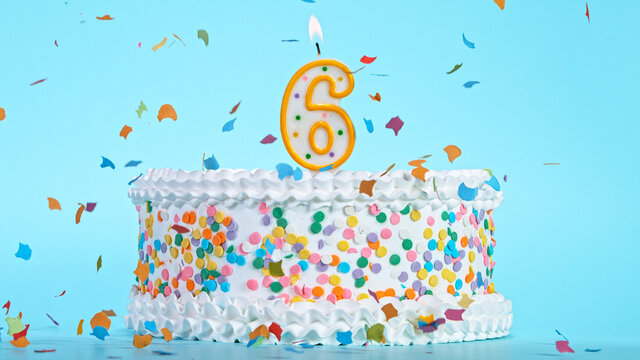 Colorful tasty birthday cake with candles shaped like the number 6. Pastel blue background.
