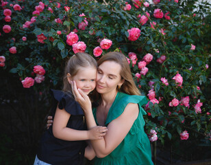 mom hugs her little daughter against the background of a rose bush