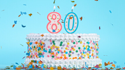 Colorful tasty birthday cake with candles shaped like the number 80. Pastel blue background.
