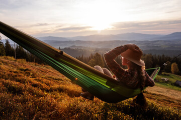 Woman hiker resting after climbing in a hammock at sunset - 438377826