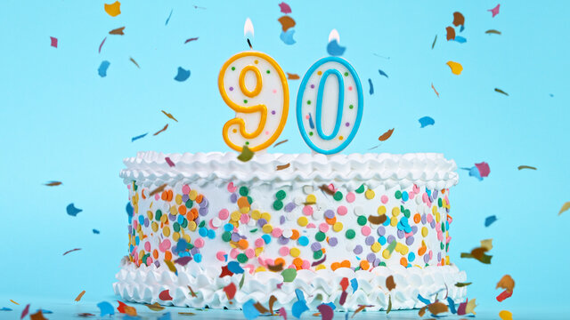 Colorful tasty birthday cake with candles shaped like the number 90. Pastel blue background.