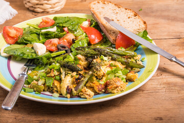 American lunch - scrambled eggs with asparagus on a plate with tomato, spinach and cheese salad. Healthy eating