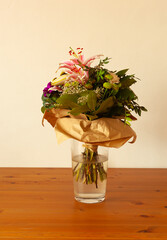 Un bouquet de fleurs dans un vase et enrobé de papier. Il y a des lys ouverts et un en bouton,...