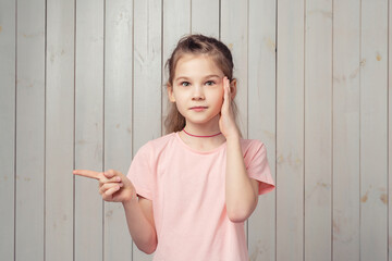 Portrait of charming little girl looking at camera and pointing fingers left, standing in pink t...