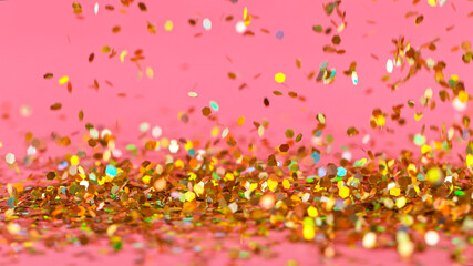 Golden glitter falling down on pink background, macro shot.