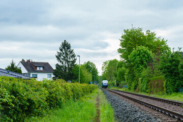 A regional train is approaching on rails on a cloudy day.