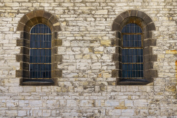 Fototapeta na wymiar Stone wall of the church with two windows with arches.