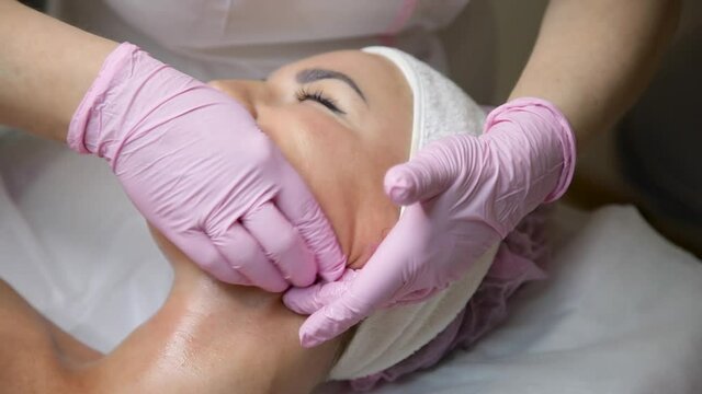 The salon specialist makes the girl a cheek massage of the face in the mouth. Buccal massage