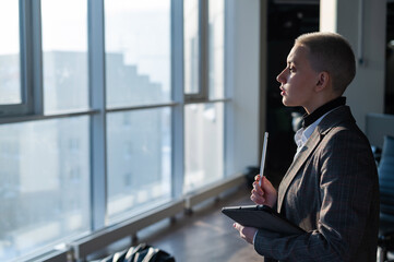 Business woman with short hair stands by the window and writes on a digital tablet with a stylus pen