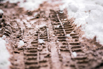 Wheel tracks on mud and snow. Snow on dirty soil with car wheel tracks. Dirty melting snow on the road. Selective focus with blurred background.
