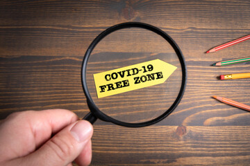 Covid-19 Free Zone. Paper arrow and magnifying glass on a wooden background