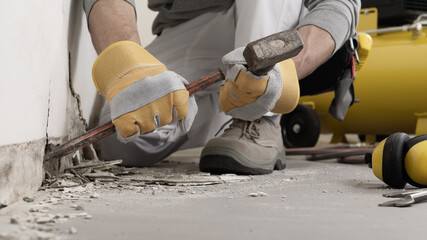 Construction worker hands with gloves working with hammer and chisel to remove old plaster from...