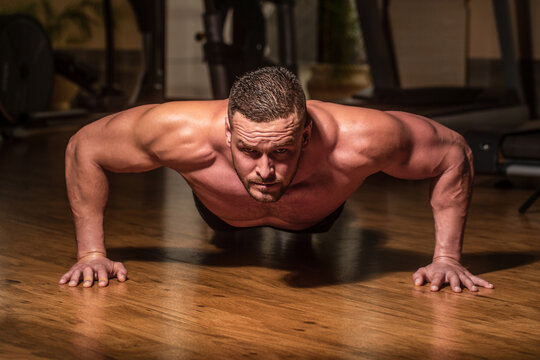 Muscular man doing push-ups on one hand against gym background. Sport. Muscular and strong guy exercising. Muscular male doing push-ups. Slim man doing some push ups a the gym. Man doing push-ups