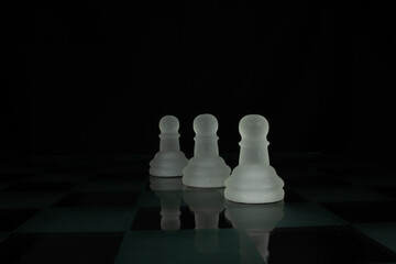 three white opaque chess piece pawns isolated on a chequered chess board with a black background