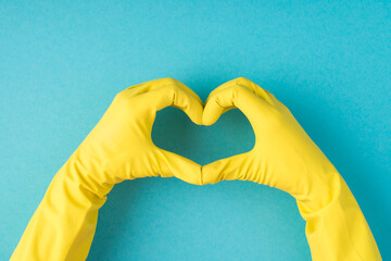 Top view photo of hands in yellow rubber gloves making heart with fingers on isolated pastel blue...