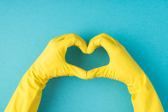 Top view photo of hands in yellow rubber gloves making heart with fingers on isolated pastel blue background with blank space