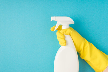 Profile photo of hand in yellow rubber glove using atomizer white detergent spray bottle without label on isolated pastel blue background with copyspace