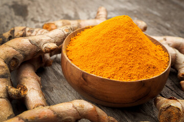 Turmeric powder and fresh turemric in wood bowls on wooden table. Herbs are native to Southeast Asia.