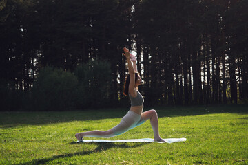 A young girl is doing yoga in the forest, outdoors on a sunny summer day. A girl stands in a rack,...