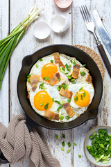 Homemade scrambled eggs with bacon and green onions in a cast iron pan, top view