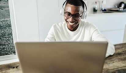 Young african man using laptop computer while wearing headphones at home - Focus on face