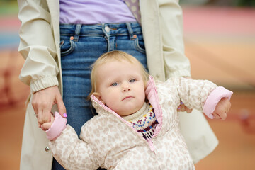 Cute toddler girl having fun on outdoor playground. Young mother is teaching her little daughter to walk. First step of baby. Walking for family with little kids.