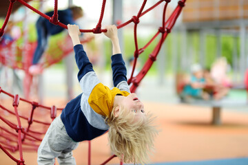 Perky preschooler boy having fun on outdoor playground. Spring/summer/autumn active sport leisure for kids. Outdoor activities for children. - obrazy, fototapety, plakaty