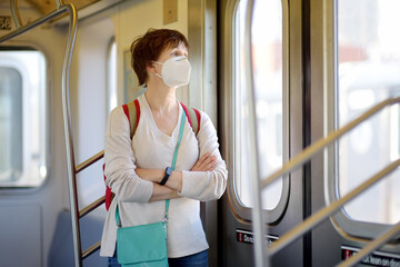 Mature woman wearing disposable medical face mask in car of the subway in New York during coronavirus outbreak. Safety in a public place while epidemic