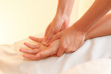 Fototapeta na wymiar Hands of female masseuse massaging woman hand palm in beauty spa salon. warm light