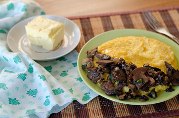 Corn porridge, fried mushrooms with onions and butter in plates on the table.
