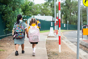 Young school kids walking along footpath with bags on