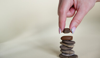 Rock balancing. A female hand on a yellow background lays small sea stones on top of each other. Balanced Stone or Balancing Rock, Zen concept. Meditation.