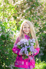 Obraz na płótnie Canvas Cute blonde girl enjoys the scent of lilacs. City walk. Spring and summer