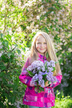Cute blonde girl enjoys the scent of lilacs. City walk. Spring and summer