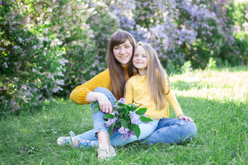 Mom and daughter laughing and hugging sitting on a blanket in the park in a clearing. The concept of a happy family, friendship, and love. Outdoor activities