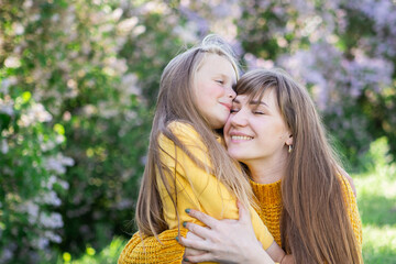 Fototapeta premium Mom and daughter laughing and hugging sitting on a blanket in the park in a clearing. The concept of a happy family, friendship, and love. Outdoor activities