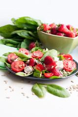 Salad with strawberries, cherry tomatoes, sunflower seeds, spinach and feta cheese on gray background