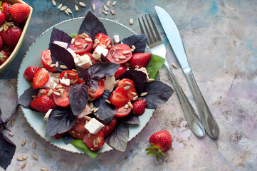 Salad with strawberries, cherry tomatoes, sunflower seeds, basil and feta cheese on gray background. Top view