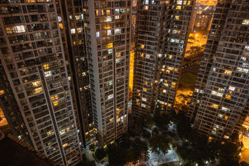 Fototapeta na wymiar Long exposure night aerial view on residential buildings complex compound. Tall skyscrapers thousands of apartments light illuminates from windows. Small square park inside community. City development