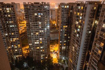 Long exposure night aerial view on residential buildings complex compound. Tall skyscrapers thousands of apartments light illuminates from windows. Small square park inside community. City development