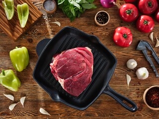 Juicy raw meat steak with salt in a grill pan. Tomatoes and spices on the wooden background
