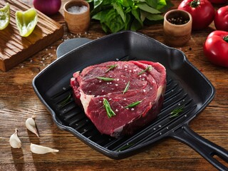 Raw beef steak with rosemary and spices on grill pan, ingredients around on a wooden table
