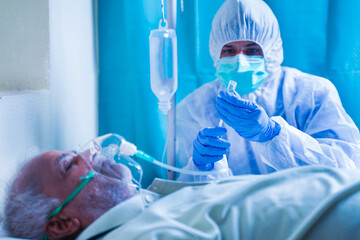 Doctor with potective suit preparing injection syringe while patient breathing on ventilator oxygen...