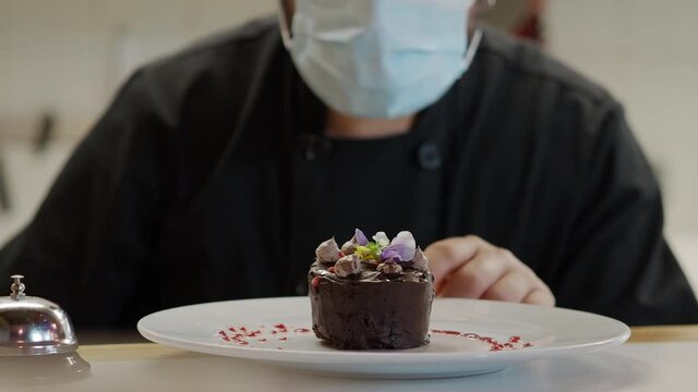 Chef with face mask decorating a cake with flowers in a restaurant. Small businesses, concept: gastronomy
