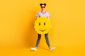 Photo of pretty funny young lady dressed striped outfit dark eyewear holding huge smiley face isolated yellow color background