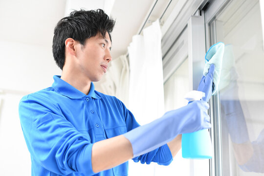 窓拭きをする清掃業のの作業服の若い男性
